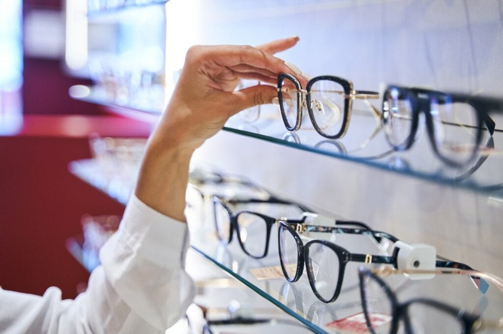 Female hand taking eyeglasses from shelf in optical store